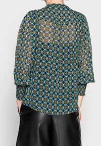 Transparent brun blus med ett geometriskt mönster av blå och svarta diamanter, smockade manschetter och rundad nederkant, designad för en avslappnad passform.