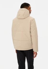 Giacca puffa beige con cappuccio, caratterizzata da un design trapuntato e una vestibilità rilassata. Texture liscia con sottili dettagli di cucitura.
