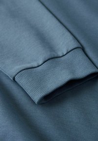 Felpa in cotone con polsini a coste, caratterizzata da una superficie liscia in una tonalità di blu attenuato, che sottolinea un design rilassato e casual.