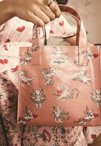 Rosa Tragetasche mit einem Cherub-Print und Herzmotiven, mit einem Etikett "Cath Kidston". Hergestellt aus glattem Material mit kurzen Griffen.