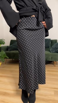 Fustă neagră cu buline, realizată dintr-un material neted, având talie ajustată și o siluetă până la genunchi, ușor evazată în partea de jos.