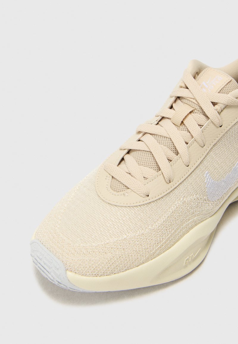 Beige Sportchuh mit strukturiertem Strickoberteil, verstärkter Zehenpartie und glatter Gummisohle mit dezenten Brandingdetails.