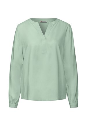 Chemisier long à manches vert clair en tissu lisse, avec un décolleté en V, une coupe décontractée et des poignets froncés. Design minimaliste sans motifs.