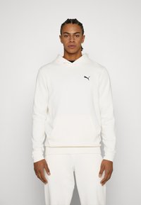 Sudadera blanca con un bolsillo tipo canguro y puños de canalé, que presenta un logo negro de Puma en el pecho. Estilo de pulóver, confeccionada con una tela suave.