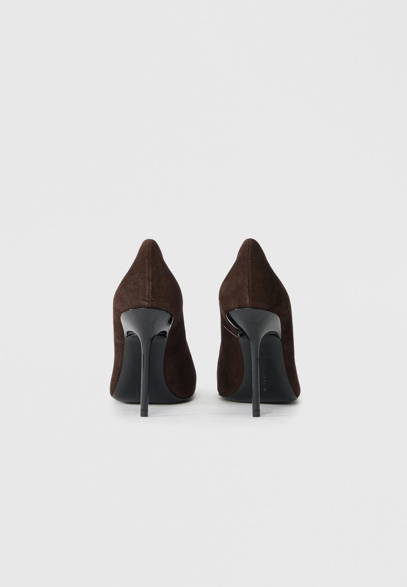 Pumps alti in suede marrone con punta affusolata e tacco a stiletto nero. Il design presenta una texture liscia e una silhouette slanciata.