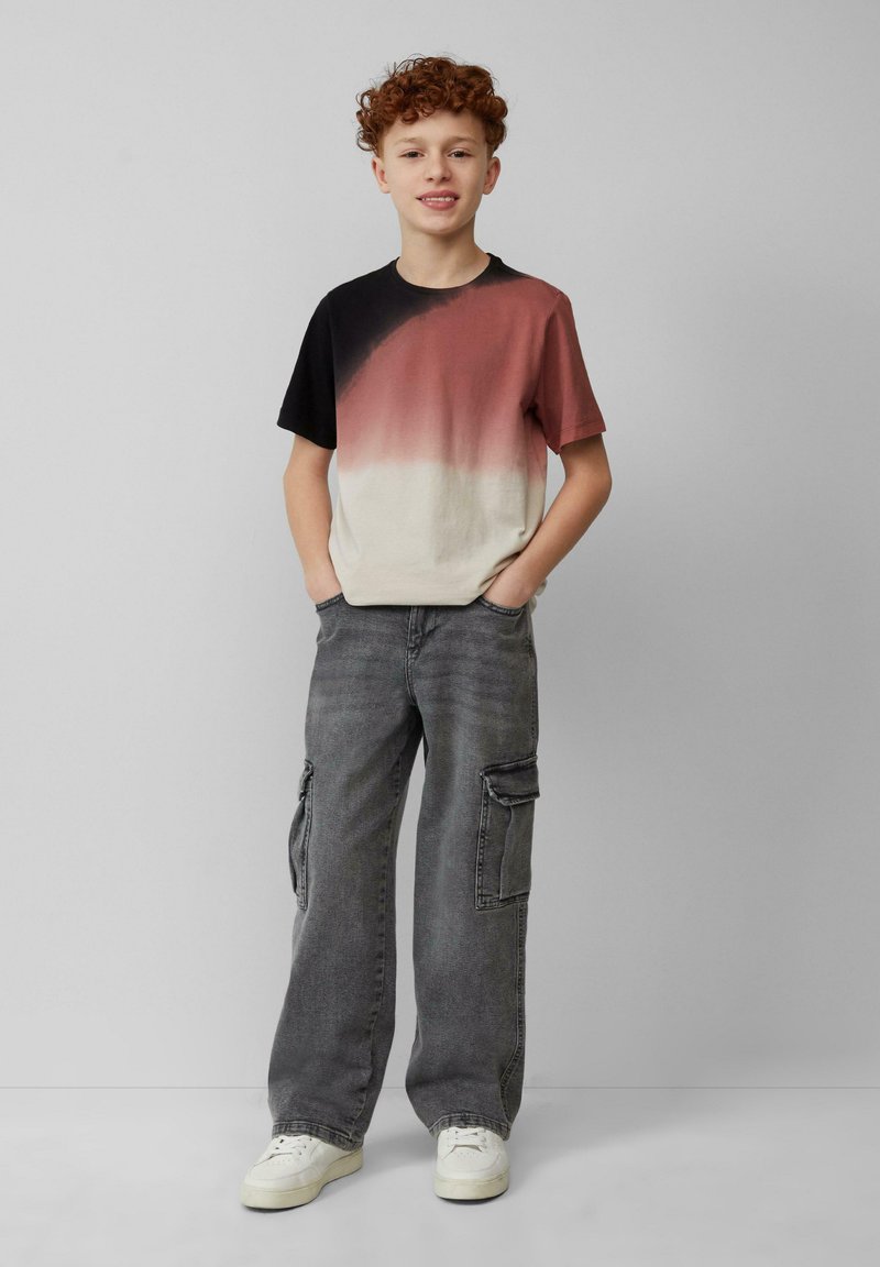 T-shirt met een rood naar zwart verloop, korte mouwen; gecombineerd met losse grijze cargobroeken met zijzakken en witte sneakers.