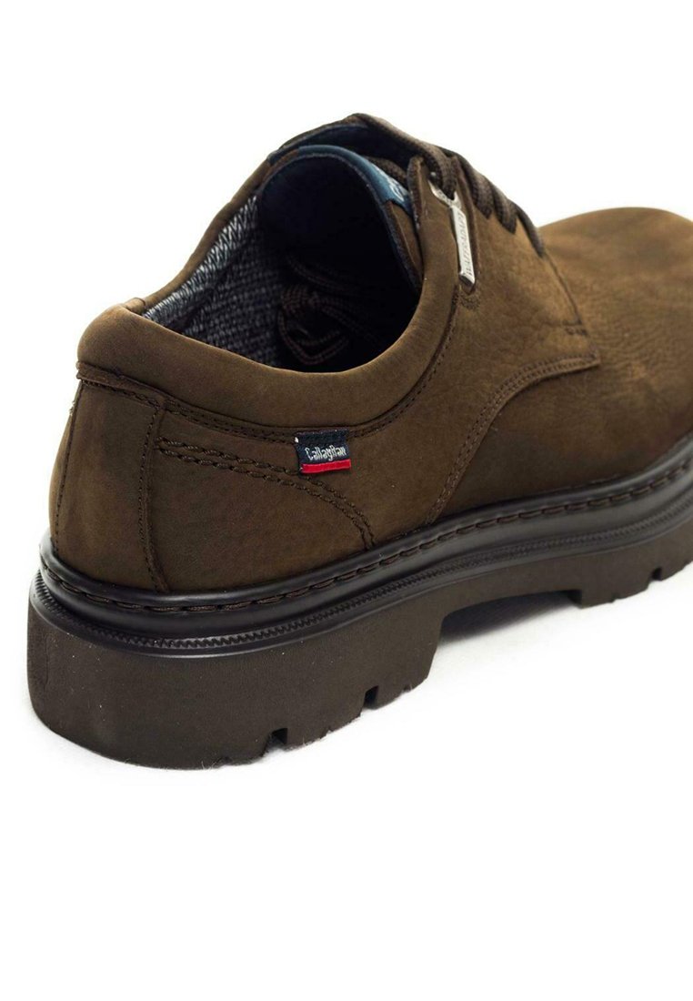 Chaussure en suède marron avec une finition texturée, bout rond, semelle en caoutchouc foncé et design à lacets. Présente une petite étiquette de marque sur le côté.