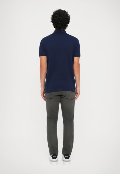 Polo de marinha com mangas curtas, tecido de algodão, combinado com jeans cinza escuro e ténis brancos com detalhes e marcação em preto.