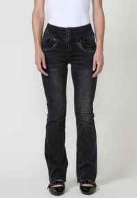 Črne jeans hlače z oprijetim pasom, petimi gumbi za zapiranje, okrasnimi žebljički na žepih in zasnovo širših hlačnic. Gladka tekstura.