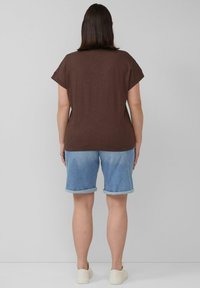 Bruine top met korte mouwen, gecombineerd met lichtblauwe denim shorts met opgerolde zoom en beige instappers. Eenvoudige en casual outfit.