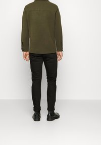 Mørkegrøn skjorteblusejakke med krave, kombineret med sorte slim-fit bukser. Jakken har manchet detaljer og en lige snit design.