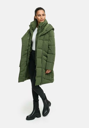 Olijfgroen pufferjack met capuchon, met geboordde secties en een ritssluiting aan de voorkant. Gecombineerd met zwarte slim-fit broek en enkellaarzen.