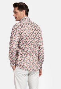 Chemise à motif floral avec des fleurs multicolores sur fond blanc, à manches longues et col classique. Pantalon blanc visible.