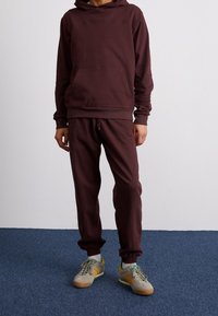 Pusero marooni, jossa on etupussitasku ja vastaavat joggerit, joissa on joustavat hihnat ja helma. Harmaat lenkkarit, joissa on vihreitä ja keltaisia yksityiskohtia.