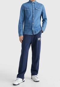 Ljusblå denimskjorta med knäppning och bröstfickor, ihopparad med marinblå sweatpants med "TOMMY"-tryck och vita sneakers.