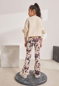 Beige sweatshirt with dropped shoulders, paired with cream flared leggings featuring a brown and purple cow print, and white sneakers.