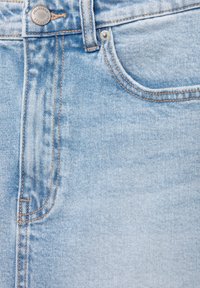 Ljusblå denimtyg med sömmar, som har en framficka, knäppning och en liten logodetalj. Bomullstextur med urtvättad effekt.