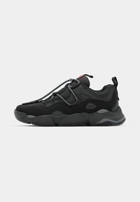 Black athletic shoe with mesh and synthetic materials, featuring prominent laces and a rugged sole design. Side view against a white background.