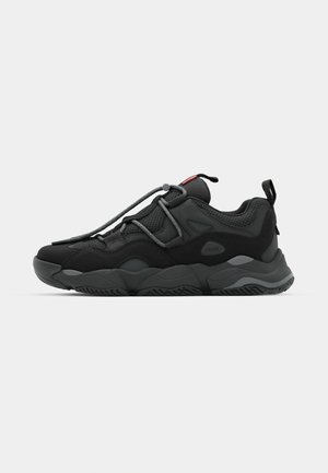 Chaussure de sport noire en matériaux mesh et synthétiques, avec des lacets bien visibles et une semelle robuste. Vue de côté sur fond blanc.