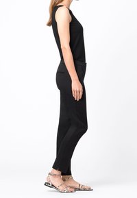 Haut sans manches noir associé à un pantalon noir slim-fit avec des détails sur les côtés, complété par des sandales à lanières avec un motif serpent.