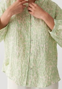 Camicia button-up verde chiaro, con texture e un motivo bianco simile a una acquerello, maniche lunghe e una vestibilità comoda. Collo arrotondato.