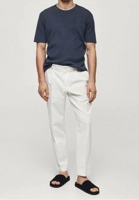 Ciemnoniebieska koszulka z krótkim rękawem, białe dopasowane spodnie i czarne klapki. Minimalistyczny design z casualowym, luźnym krojem.