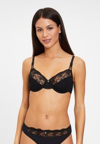 Zwarte kanten beha en bijpassende slipset met bloemenkantaccenten, verstelbare banden en een strikdetail in het midden. Gladde stof met doorzichtige overlay.