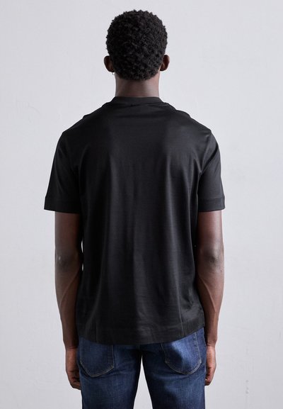 T-shirt en coton noir à manches courtes, encolure ronde et coupe décontractée. Porté avec un jean en denim bleu. Tissu texturé, finition lisse.