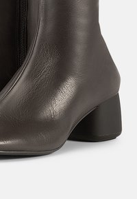 Καφέ δερμάτινο μποτάκι αστραγάλου με στρογγυλεμένη μύτη, υφή στην επιφάνεια και χαμηλό τακούνι σε σχήμα πλίνθου. Διαθέτει πλευρικό φερμουάρ για εύκολη εφαρμογή.