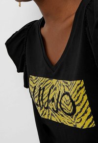 Maglietta nera con maniche a sbuffo, caratterizzata da una scollatura a V e una grafica di zebra gialla e nera con dettagli in strass sul davanti.