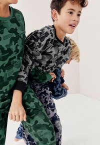 Des enfants portant des vêtements d'intérieur à motif camouflage ; les couleurs incluent le vert, le gris et le bleu. Tissu doux avec des poignets côtelés et des accents de texte imprimé.