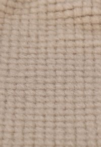 Beige strukturerad tyg med ett rutmönster, som har en mjuk och lurvig yta. Ytan verkar varm och inbjudande med en jämn finish.
