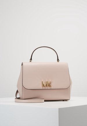 Beżowa skórzana torebka z górnym uchwytem, odpinanym paskiem na ramię i złotym logo MK na przedniej klapie, umieszczona na białym piedestale.