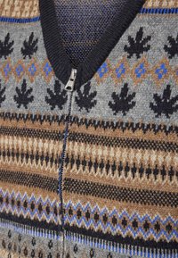 Šedý vzorovaný svetr na zip s černým žeberným límcem. Obsahuje složité vzory v hnědé, modré a černé barvě přes různé texturované pruhy.