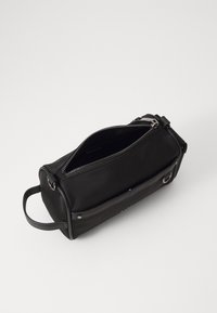 Borsa cilindrica nera in tessuto con chiusura a zip, dettagli in pelle e manico laterale. L'interno è spazioso e privo di rivestimento.