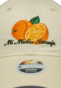 Beige verstelbare pet met borduursel van een sinaasappel en een citroen met groene bladeren. De tekst eronder luidt "Mi Media Naranja" in groene draad.