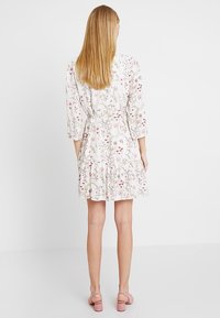 White floral dress with three-quarter sleeves, cinched waist, ruffled hem, and pink floral patterns. Paired with pink heeled sandals.
