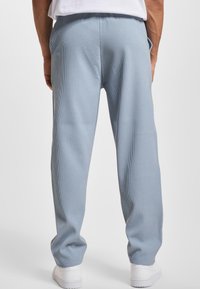 Pantalones de canalé azul claro con cinturilla elástica y bolsillos laterales, corte ajustado y puños en los tobillos. Combinados con zapatillas blancas.