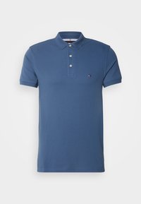 Polo bleu à manches courtes avec trois boutons et un petit logo sur la poitrine gauche, présenté sur un fond uni.