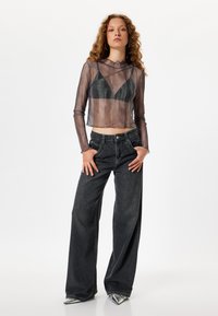 Haut transparent à manches longues avec décolleté arrondi superposé à un soutien-gorge sombre, associé à un jean large taille haute de couleur sombre et des chaussures métalliques à bout pointu.