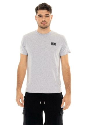 Un homme porte un tee-shirt Leone gris clair avec un petit logo sur la poitrine et un short cargo noir, sur fond blanc.