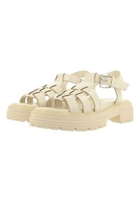 Sandales compensées épaisses couleur blanc cassé avec plusieurs brides et fermetures à boucles argentées, vues de face et de côté sur fond blanc.