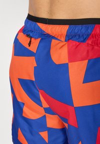 Swim shorts featuring an abstract design in blue, orange, and red. Made of lightweight fabric with an elastic waistband and drawstring.