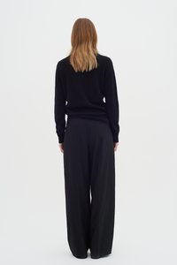 Pulover negru și pantaloni largi negri, ambele având o textură moale. Ținuta este minimalistă, cu o siluetă curată și fără modele vizibile.