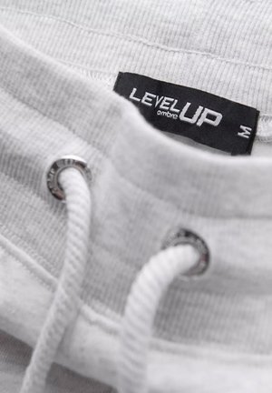 Weißer Sweatshirtkragen mit silberner Öse, weißem Kordelzug und schwarzem "LEVEL UP"-Label. Texturiertes Gewebe und gerippte Details sichtbar.