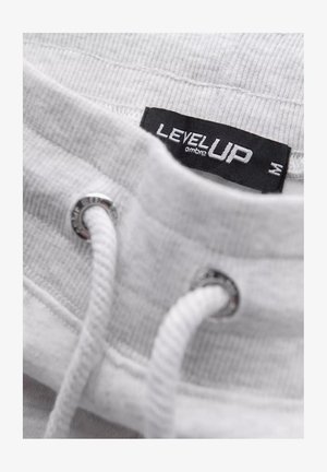 Bílá mikina s límečkem a stříbrným okem, bílou stahovací šňůrou a černou etiketou "LEVEL UP". Viditelná texturovaná tkanina a žebrované detaily.