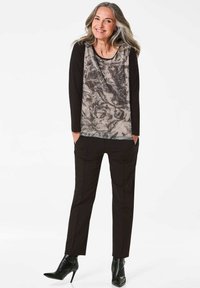 Zwarte langslobige top met een getextureerd, grijs bloemenpatroon en zwarte broek. Het model draagt puntige zwarte enkellaarsjes.