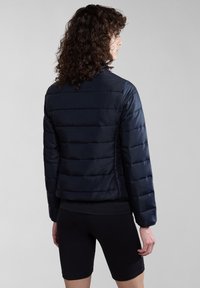 Marineblauwe pufferjack met horizontale stiksels, elastische manchetten en zijschuiten. Draagt over een zwarte top en shorts. Minimalistisch ontwerp.