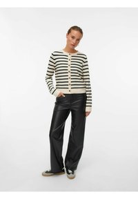 Cardigan rayé en crème et noir, avec un col rond, des boutons, des manches longues et une coupe ajustée. Associé à un pantalon en cuir noir.