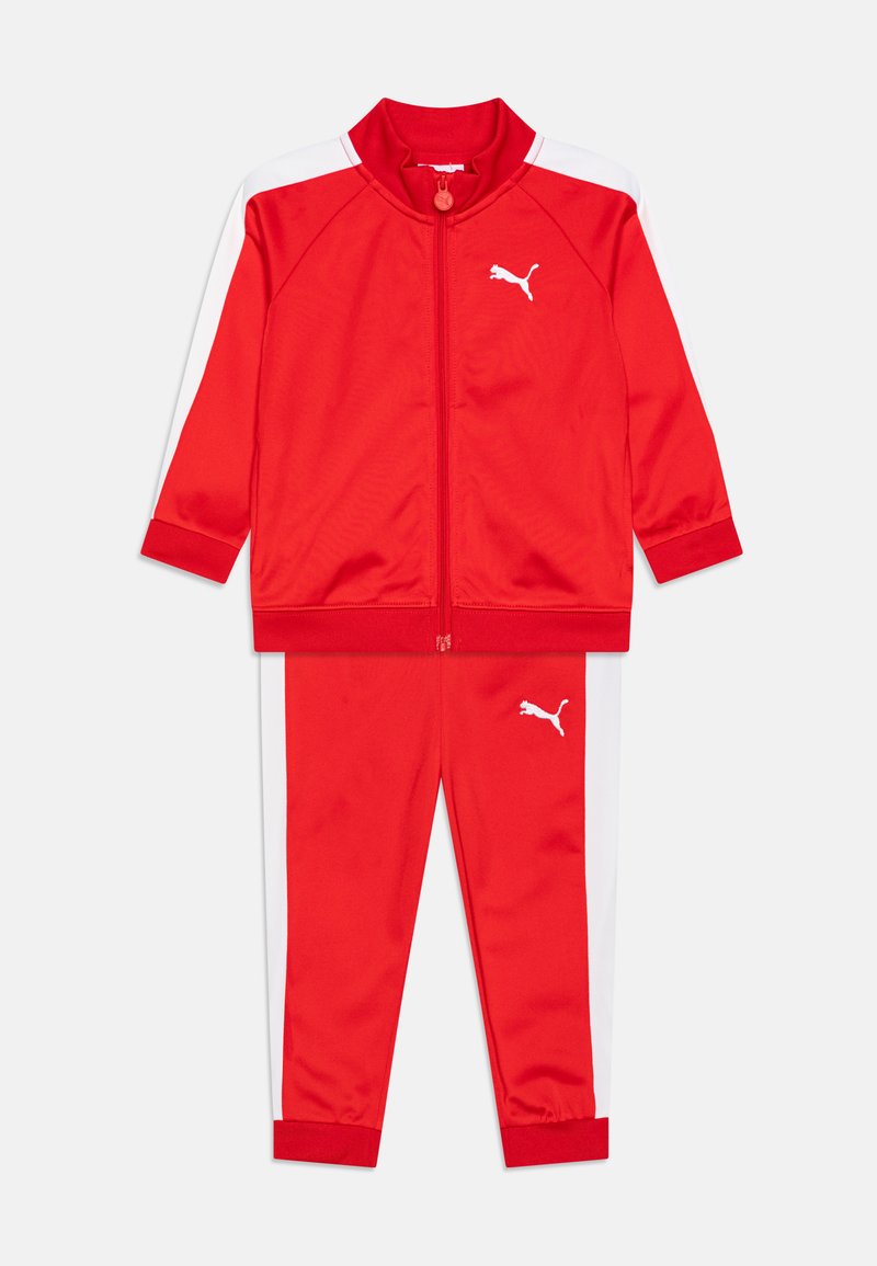Survêtement rouge en tissu lisse. Comprend une veste zippée avec des rayures blanches et un pantalon assorti, tous deux ornés d'un logo blanc.